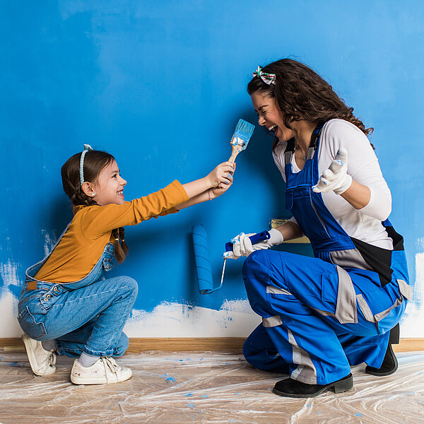 Mutter und Kind lachen und bemalen Wand mit blauer Farbe