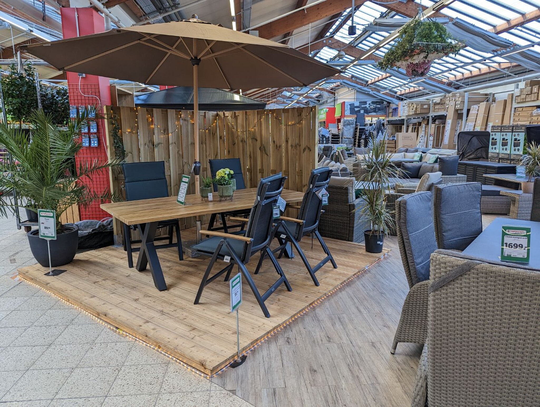 Verkaufsfläche mit Gartenmöbeln Musteraufbau Terrassendielen mit braunem Trenner aus Holz und Sonnenschirm 