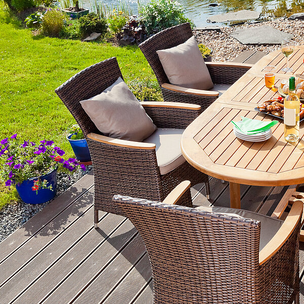 Holztisch sowie Gartensessel mit Kissenauflagen auf Terrasse mit Blick auf garten